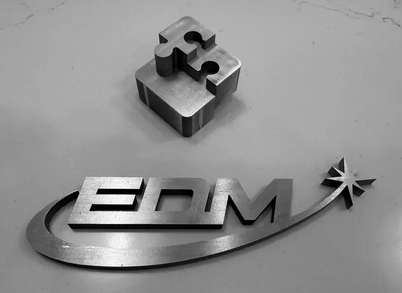 The Space Coast EDM logo and a puzzle-piece test part, both wire-cut from metal plate